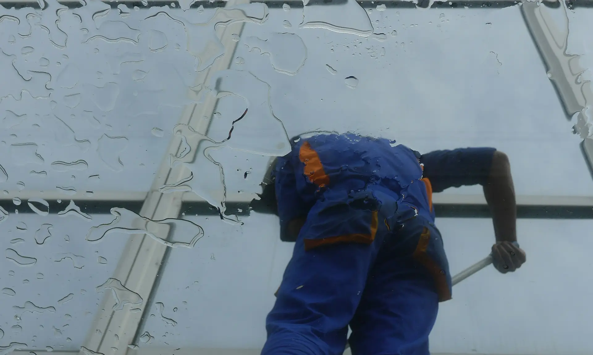 Fensterputzer reinigt ein großes Glasdach, gesehen von unten durch die nasse Scheibe