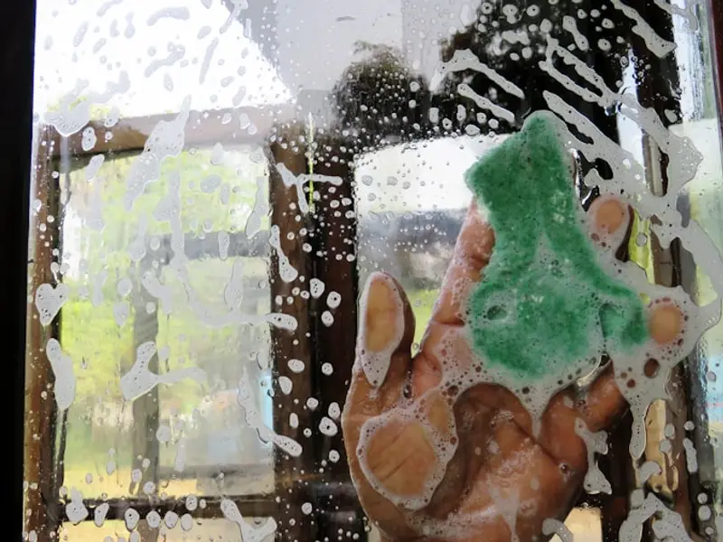 Hand mit Schwamm seift eine Fensterscheibe ein